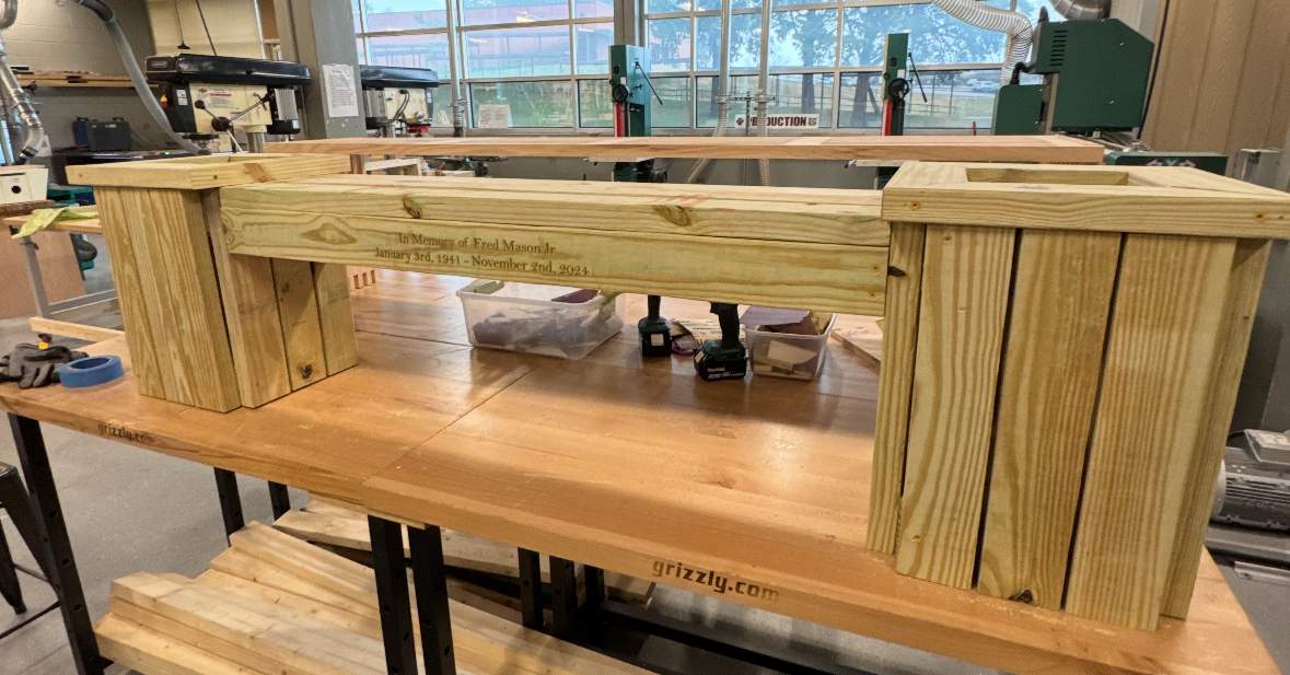 A lush middle school garden, featuring raised beds with various plants like tomatoes, squash, and corn, with a wooden bench in the foreground